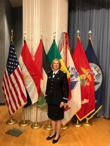 Lady in Military Unifrom in front of the US Flag and Armed Forces flags