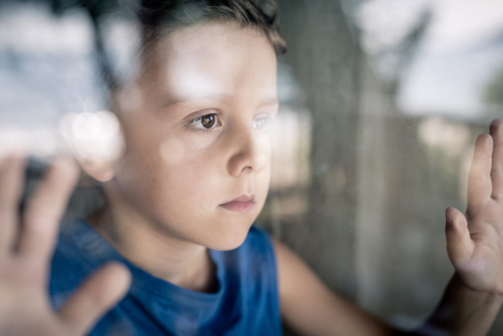 One sad little boy standing near the window at the day time. Concept of sorrow.